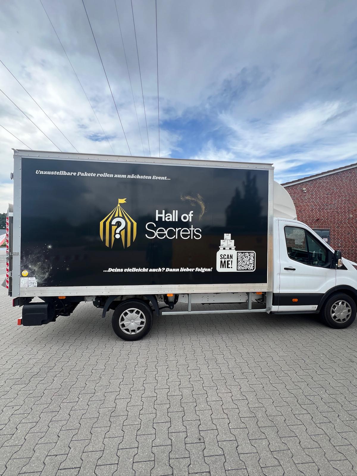 Ein weißer Hall-of-Secrets-LKW mit schwarz-goldenem Aufbau und großem Hall-of-Secrets-Logo.